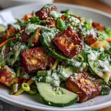 A close-up view of Creamy Asian Cucumber Salad with Crispy Tofu shows glistening tofu and fresh herbs on a ceramic plate, perfect for a light vegetarian lunch.