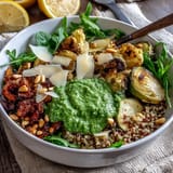 Fresh arugula greens topped with warm grains and shaved Parmesan in a healthy Arugula Pesto Bowl.