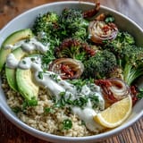 Golden crispy roasted broccoli over fluffy quinoa with creamy tahini sauce in a white ceramic bowl.