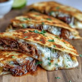 Tender shredded beef birria stuffed inside golden quesadillas, paired with a rich, spicy consommé for dipping and celebrating.