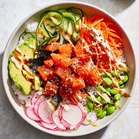 This deconstructed sushi bowl features marinated fish, edamame, and fresh vegetables drizzled with spicy mayo and sesame seeds.