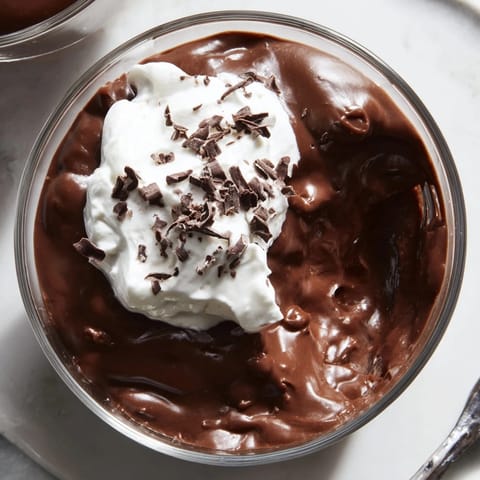 Creamy chocolate pudding in a glass topped with chocolate shavings and fresh raspberries.