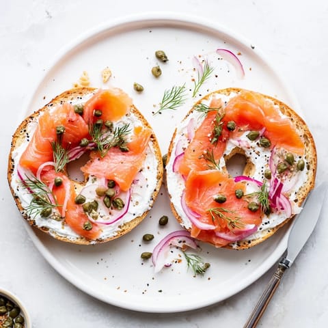 Toasted sesame bagel generously spread with cream cheese, featuring sliced tomato and cucumber for a fresh bite.