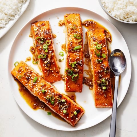 Tender pan-seared Honey Garlic Salmon fillets with a sticky sauce and fresh green onion garnish, resting on a white plate.