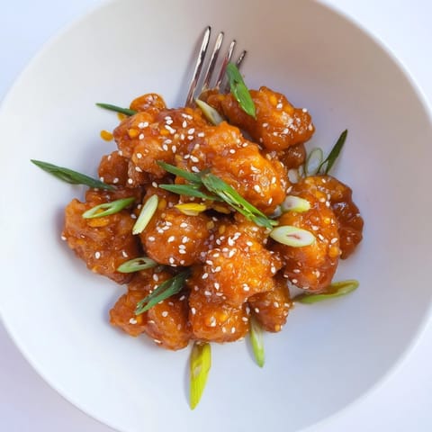 Glossy, tangy orange sauce coats golden fried chicken pieces, with bright citrus zest and sesame seeds.