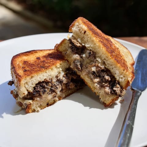 Truffle Grilled Cheese bubbling with melted Gruyère, sliced on a wooden cutting board.  
