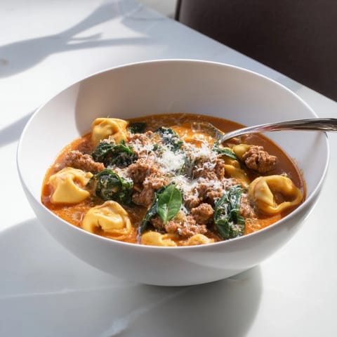 Creamy Tuscan Tortellini Soup served in a rustic bowl, featuring Italian sausage, wilted spinach, and fresh basil garnish. 