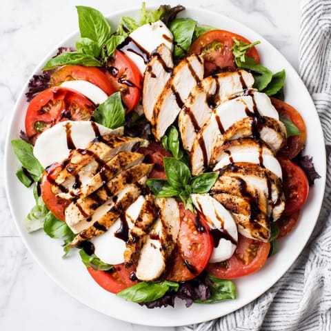 Sliced tomatoes and mozzarella on a platter with juicy grilled chicken and basil leaves, a perfect light summer dinner.