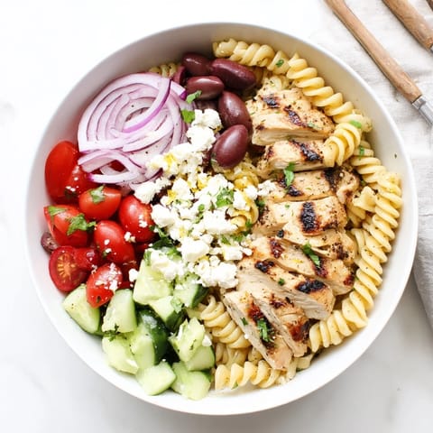 Close-up of a Greek Chicken Pasta Bowl featuring crumbled feta, crisp cucumbers, and fresh parsley garnish.
