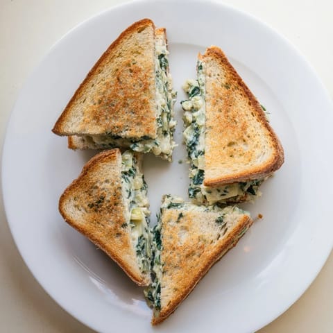 Golden-brown sourdough grilled cheese sandwiches with spinach and artichoke filling, melted and ready to serve.