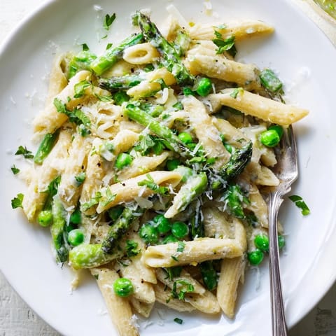 Freshly cooked Garlic Parmesan Spring Vegetable Pasta in a white bowl, showcasing tender asparagus, peas, and green beans coated in a light, creamy sauce.  