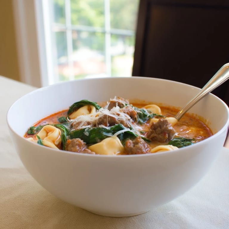 Hearty Tuscan Tortellini Soup with swirls of cream, colorful vegetables, and crusty bread on the side for dipping.