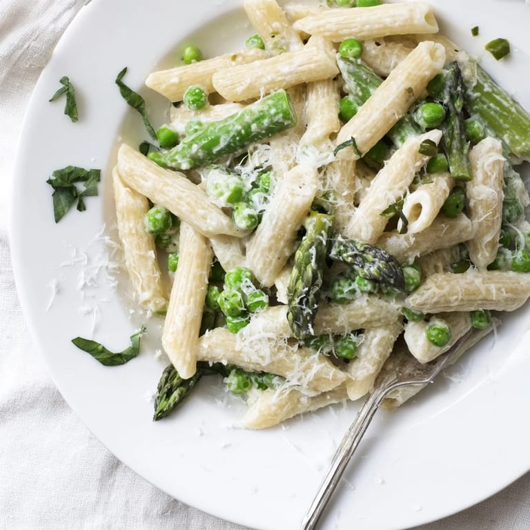 Bright spring pasta dish with al dente penne, vibrant green vegetables, and melted Parmesan, garnished with fresh basil leaves.  