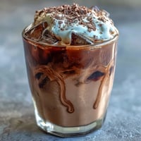 Velvety chocolate cream floats atop chilled cold brew coffee in a tall glass, garnished with chocolate syrup drizzle.